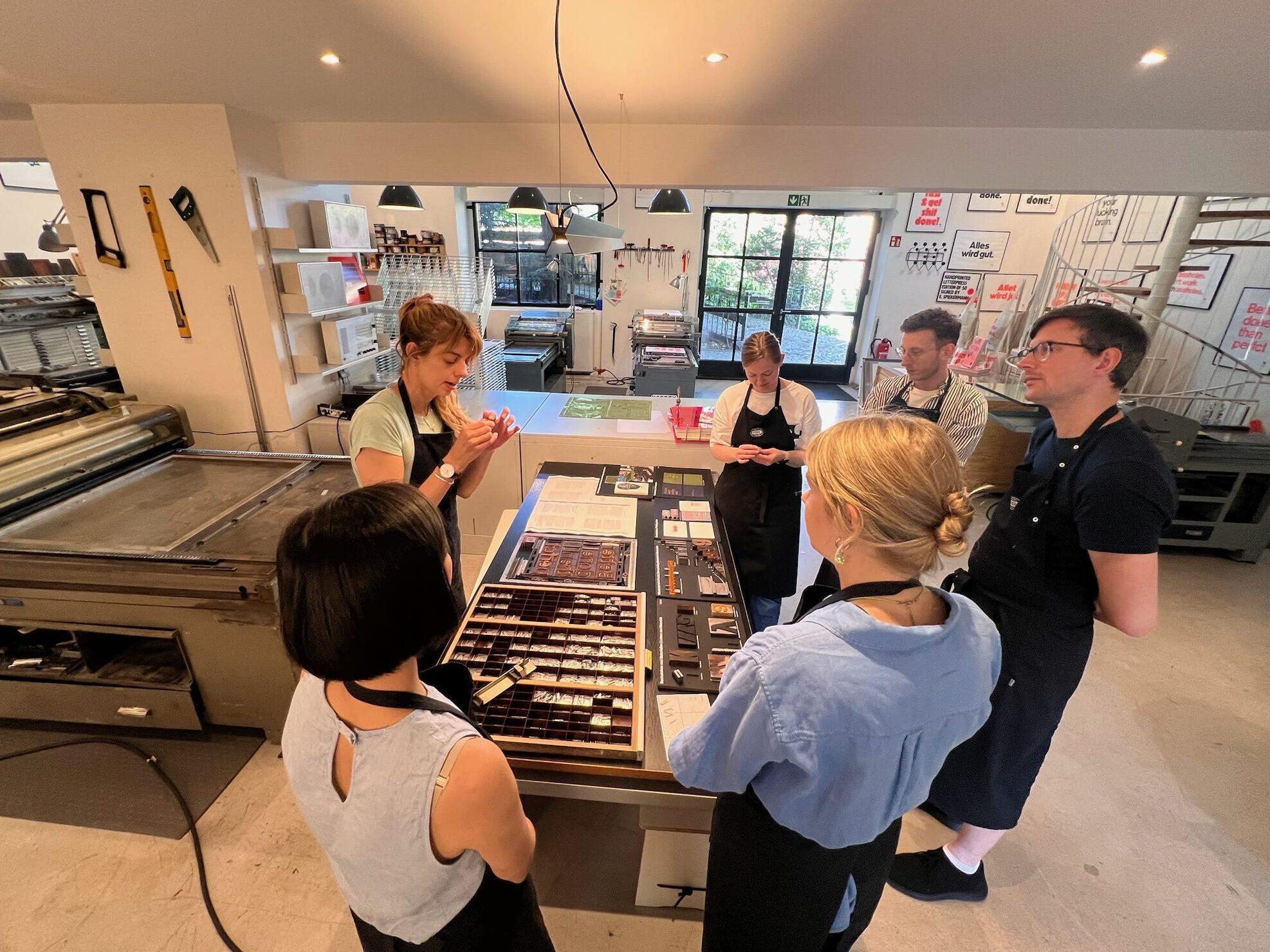 Photo of a group of people standing around a desk, looking at metal type samples, intently listening to one person explaining