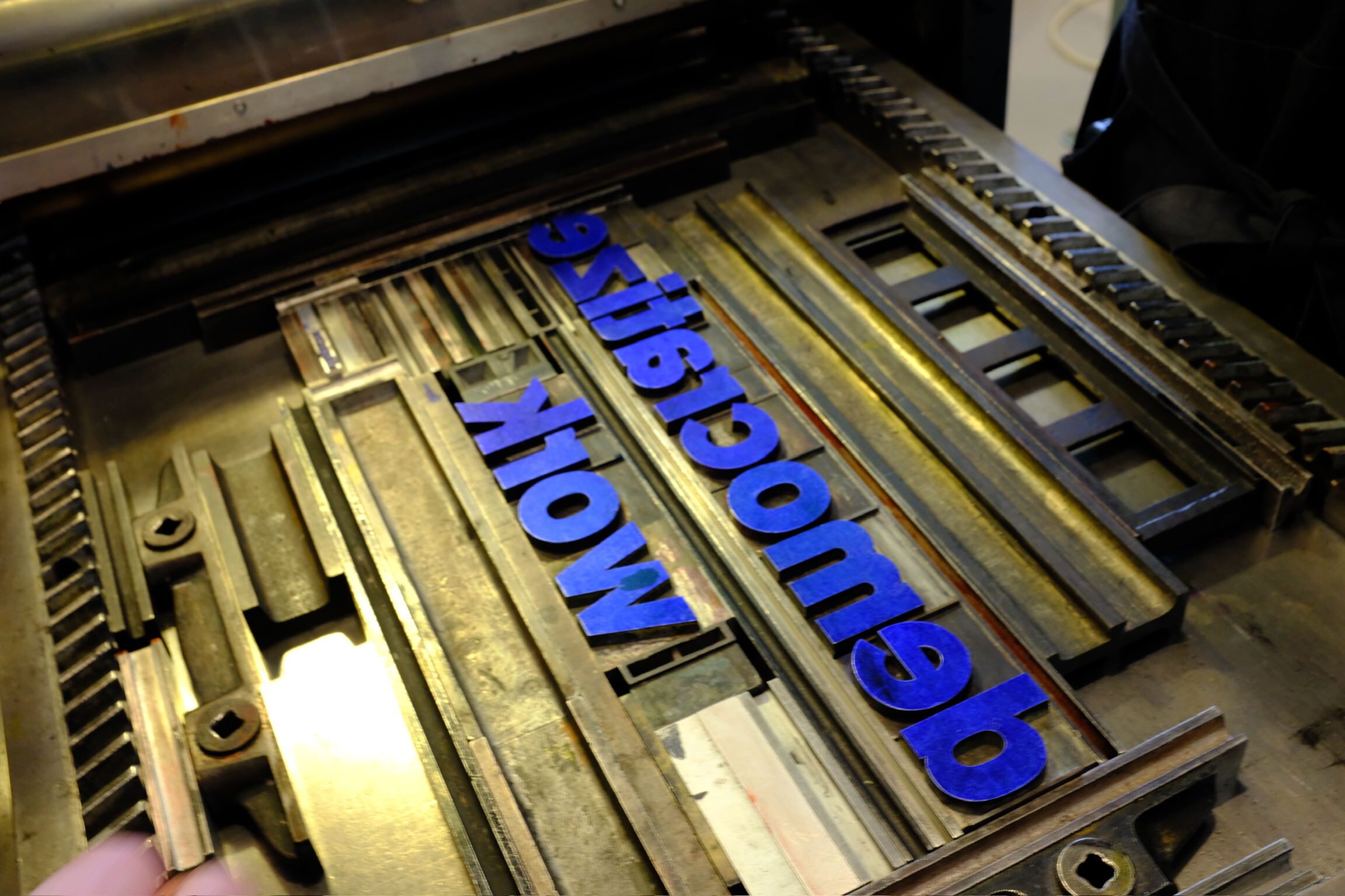 Photo of the words “democratize work” arranged in metal type in a frame, with blue ink applied