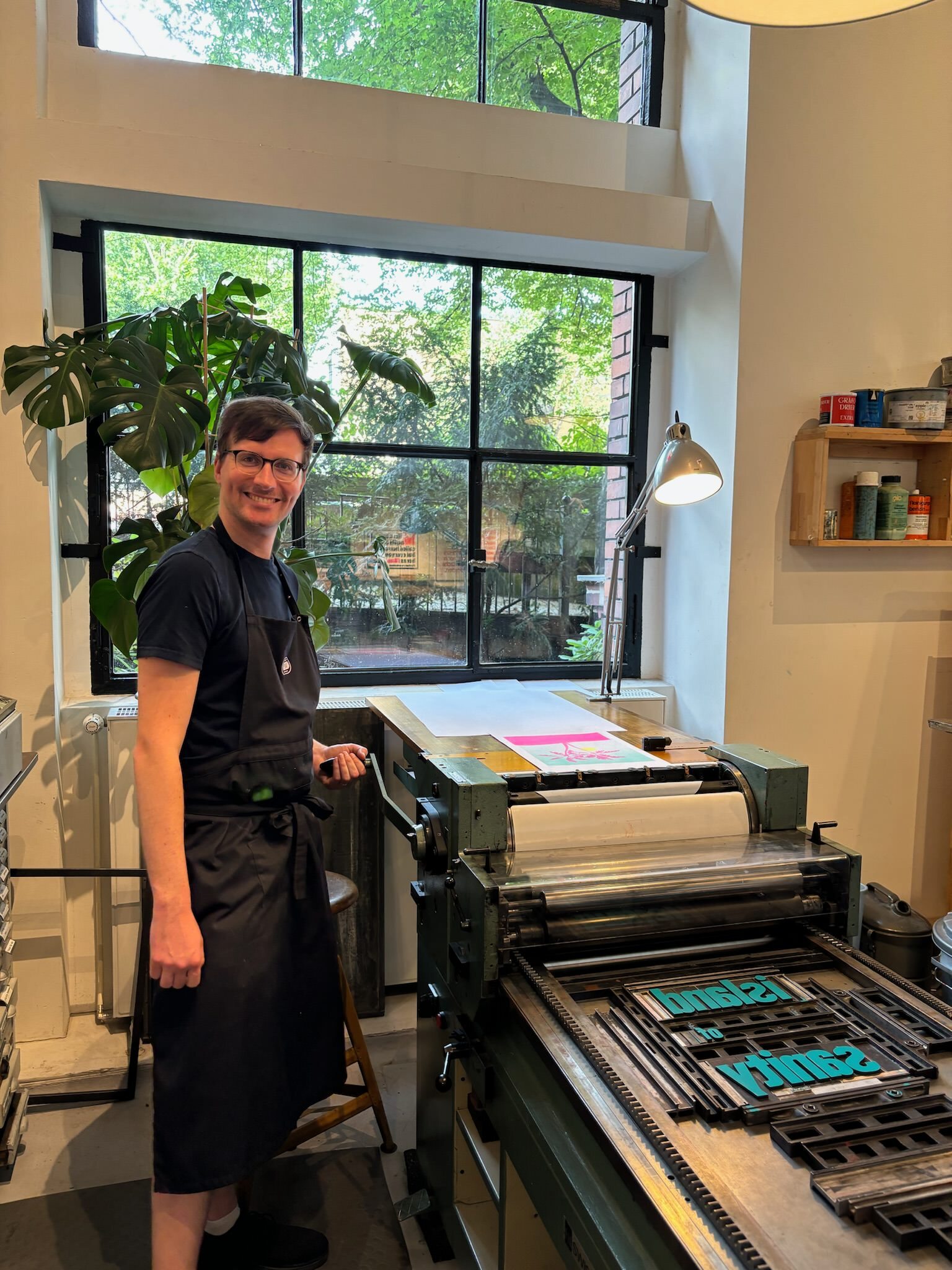 Photo of a dude standing next to a printing machine, ready to turn the crank and roll the paper