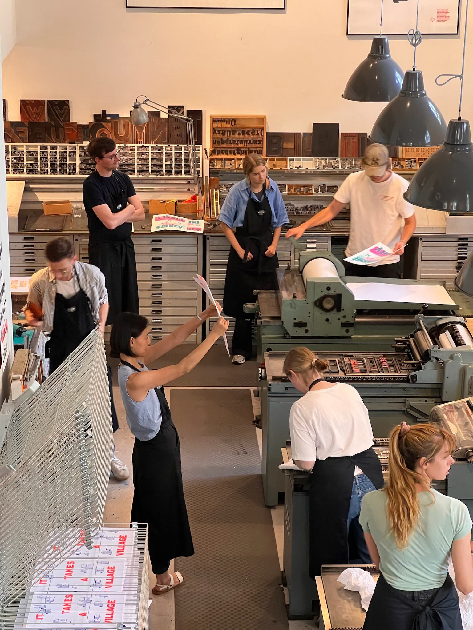 Photo of several people standing around a letterpress workshop, looking at posters, everyone is very busy and in the moment