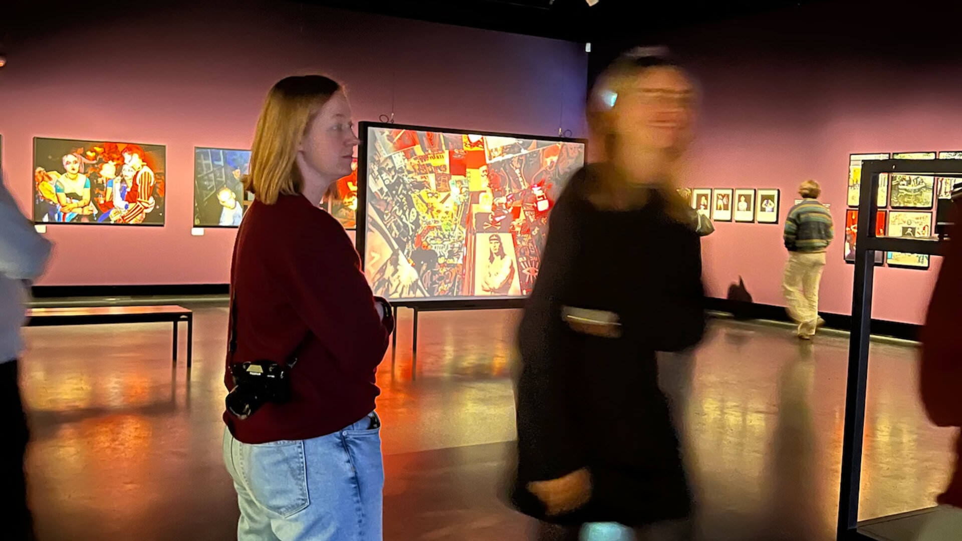 Photo of two people standing in an art gallery with large photo prints on the walls, dimly lit, one person blurry in motion