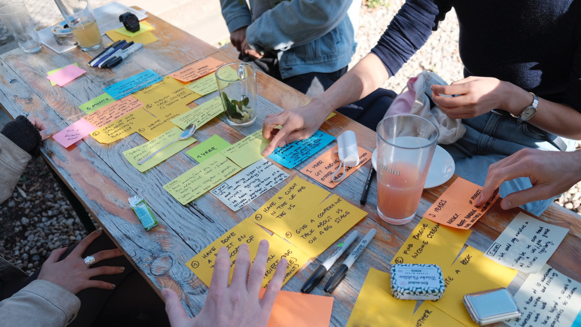 Photo of benches outside with lots of colorful sticky notes on top and people sitting around, doing an exercise of goal planning