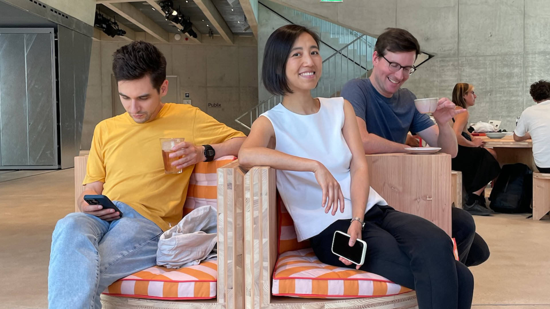 Photo of three people sitting in a café, laughing and smiling at the camera, while drinking coffee and tea