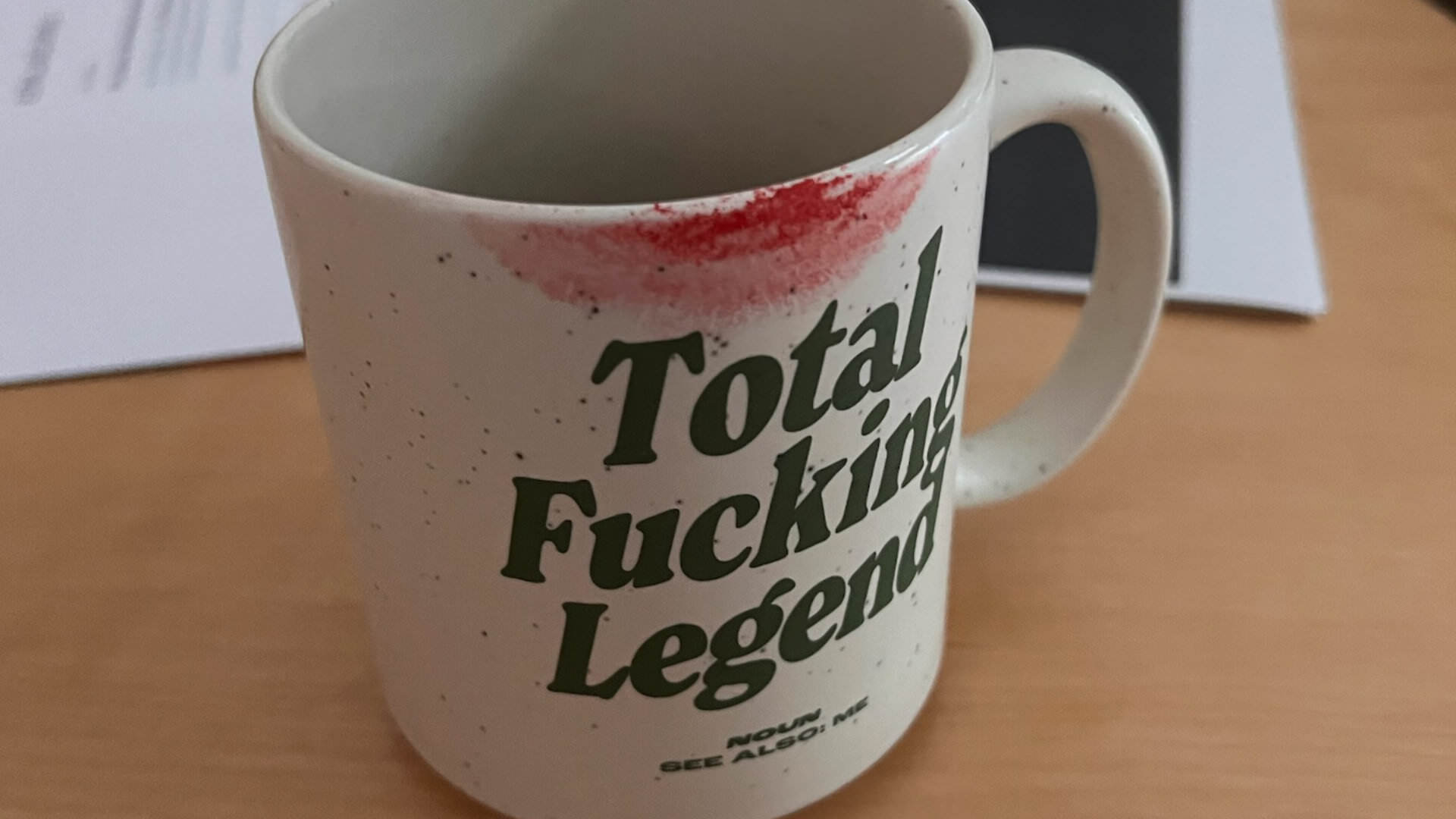 Photo of a coffee mug that says “Total Fucking Legend“, with red lipstick smeared around the top from drinking