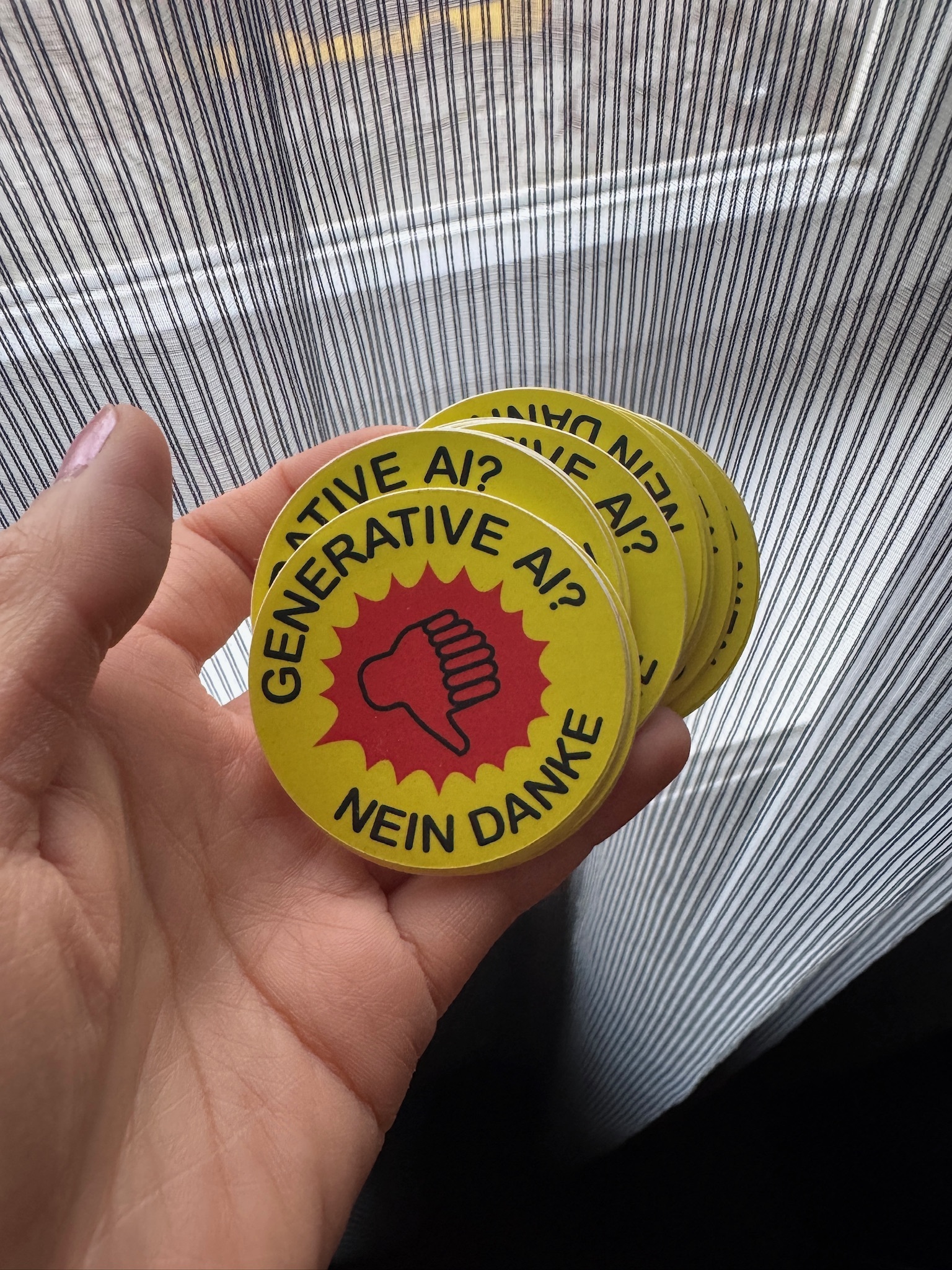 Photo of a hand holding a bunch of stickers with a thumbs-down symbol and the text “Generative AI? Nein Danke” around it