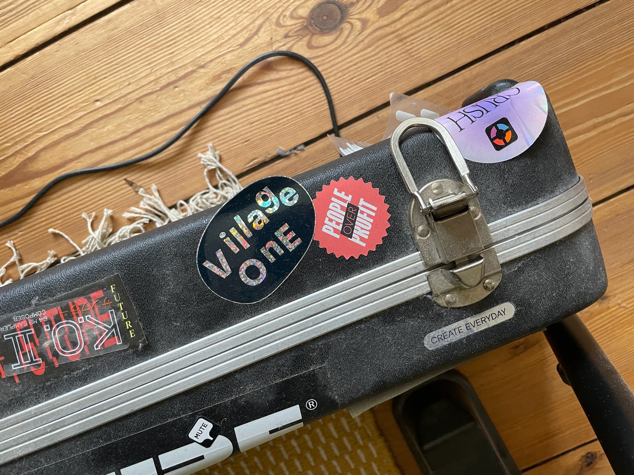 Photo of a suitcase with a few stickers on it, the two central ones saying “People over Profit” and “Village One”